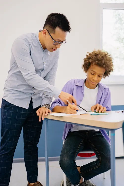 Teacher guiding a teen student at his desk during a science lesson