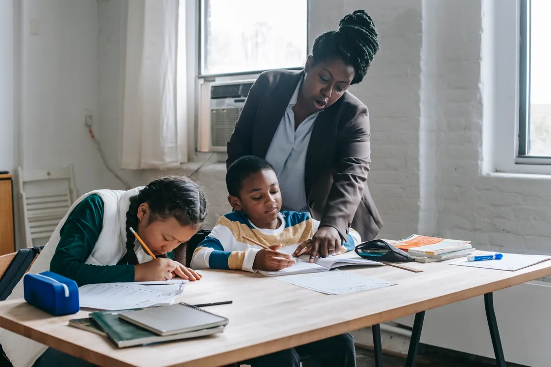 Teacher helping two students with their schoolwork at a table in a bright classroom