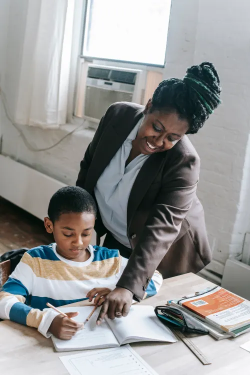 Teacher smiling and pointing at a boy's notebook to explain the next step